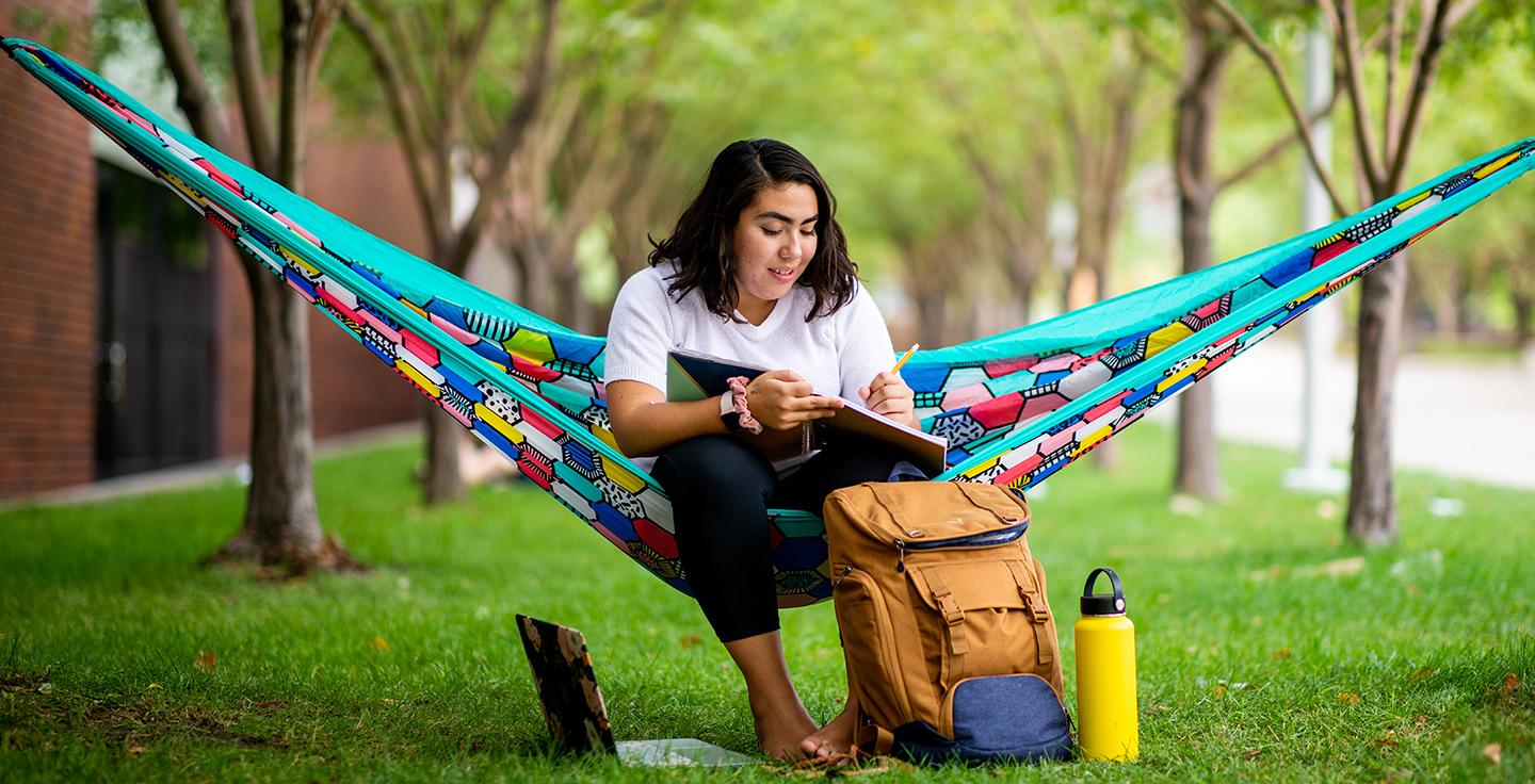 A student studying on a hammock outdoors.